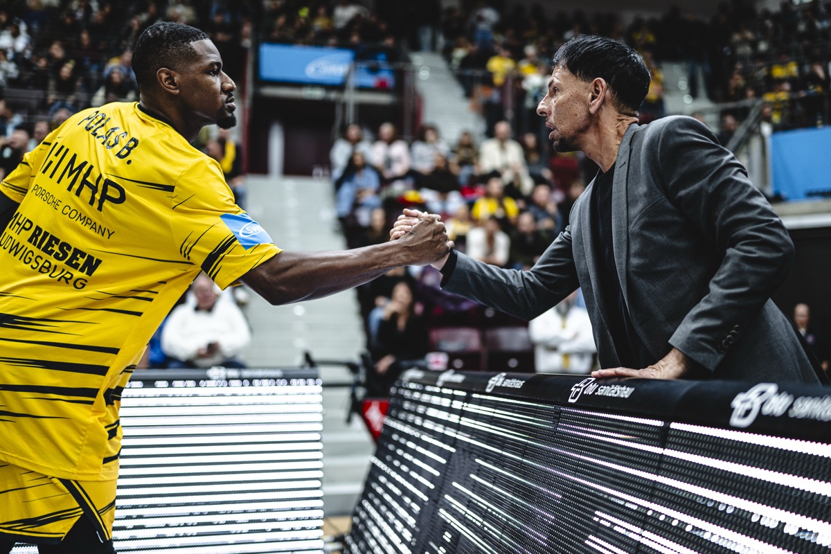 Vor dem Spiel: Spieler im Warm-up-Shirt begrüßt einen Mann im Anzug an der LED-Bande